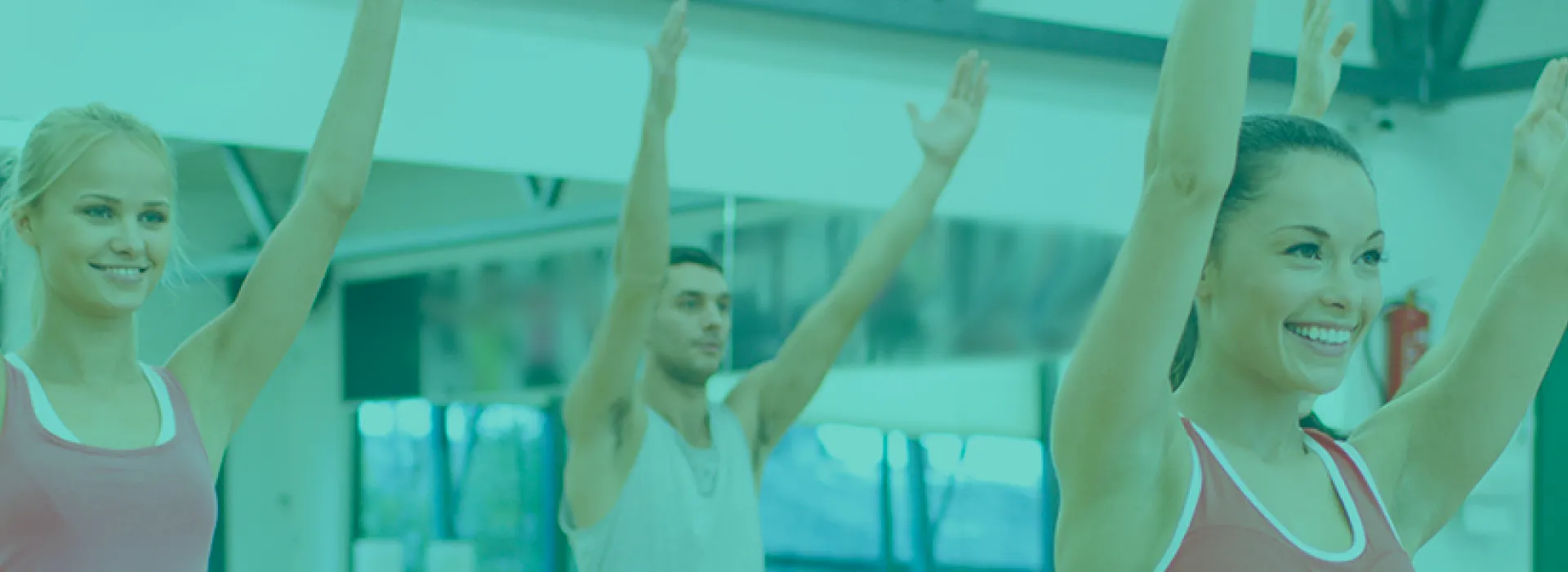 Yoga class with smiling women and one man stretch upwards in a group fitness room with mirror behind them