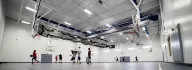 Large back gym with blue flooring and teenagers playing basketball