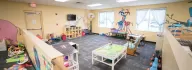 Empty child care room with animals on the wall, train tracks on table, rocking chair and cubby holes for kid's personal items