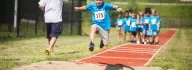 Young boy at University of Dayton's Welcome Stadium, in midair doing a long jump into a sandpit at YMCA's Day Camp Olympics