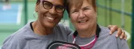 Two women wearing matching gray t-shirts for the YMCA Senior Showcase, holding a pickleball paddle and smiling together