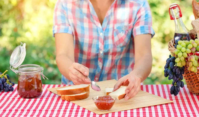 A woman putting jelly on bread on a picnic blanket