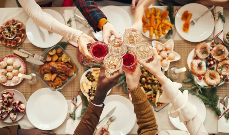 A holiday table of food with people holding up their glasses