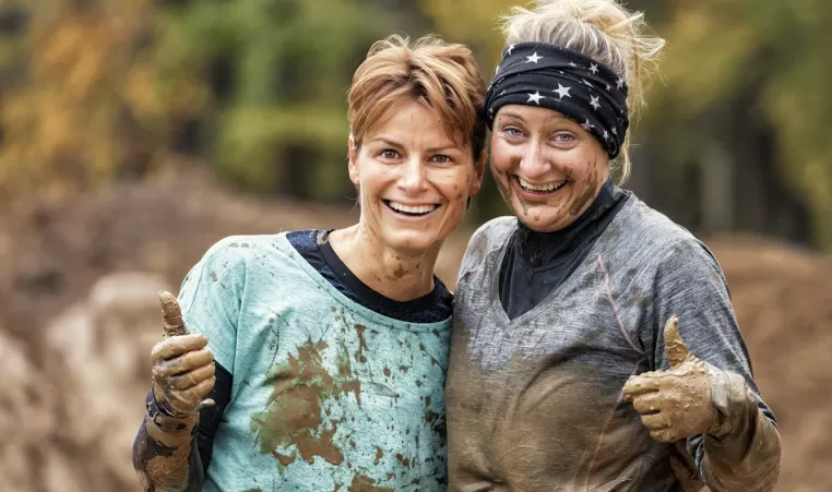 Two women covered in mud giving a thumbs up