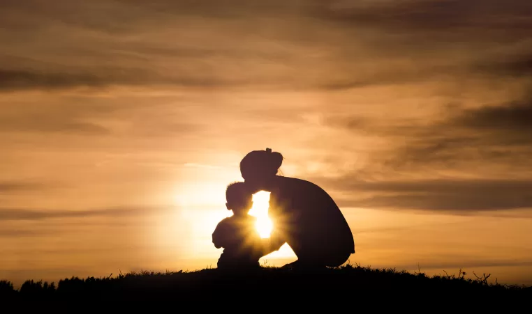 Silhouette of a young mother lovingly kissing her little child