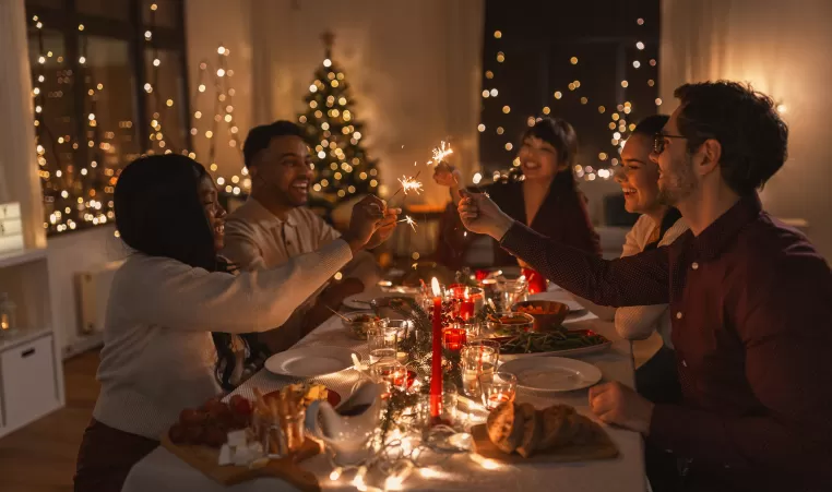 holidays and celebration concept - multiethnic group of happy friends with sparklers having christmas dinner at home