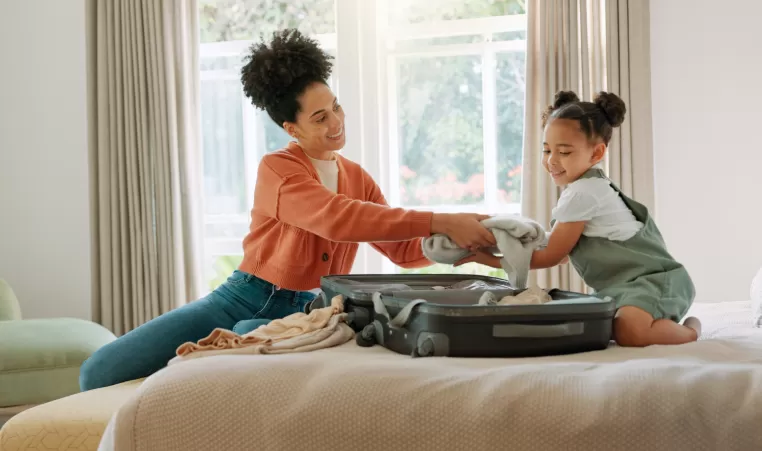 Travel, luggage and mom packing with child in bedroom getting ready for trip. Helping hands, black family and young girl help mother pack clothes in suitcase for holiday, vacation and weekend