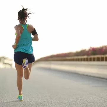 A woman running outside with an aqua racer back tank top on a sunny morning