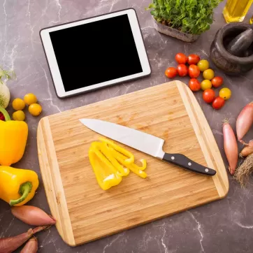A cutting board in a kitchen surrounded by vegetables