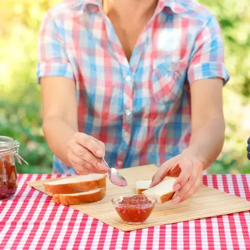 A woman putting jelly on bread on a picnic blanket