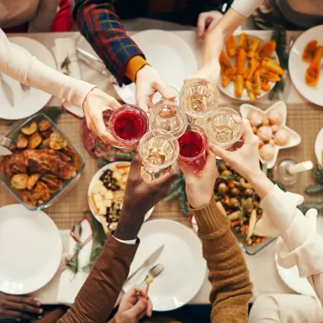 A holiday table of food with people holding up their glasses