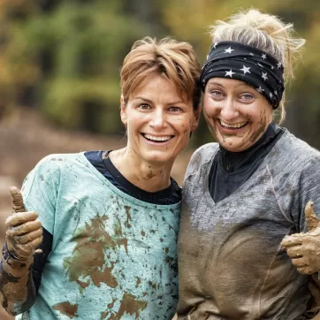 Two women covered in mud giving a thumbs up