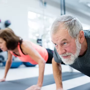 Senior couple in gym working out, doing push ups