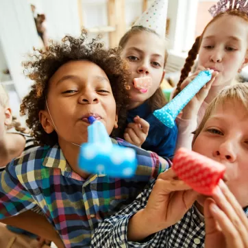 High angle view at multi ethnic group of children blowing party horns at camera