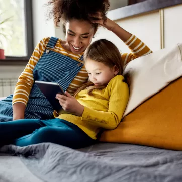 Quality childcare matters. African american woman baby sitter and caucasian cute little girl smiling, using tablet pc, sitting at home. Children education, leisure activities, babysitting concept