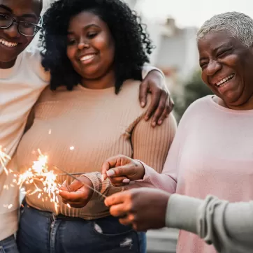 Happy black family celebrating with sparklers outdoor at home - Focus on mother face