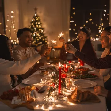 holidays and celebration concept - multiethnic group of happy friends with sparklers having christmas dinner at home