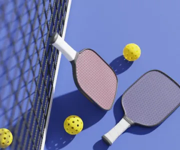 Pickleballs and pickleball paddles laying on a court