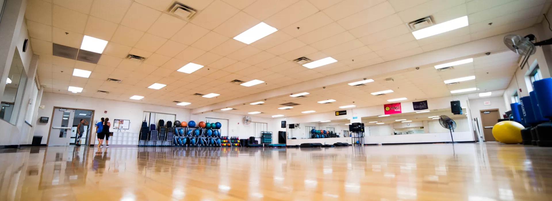 Large group exercise room shot from the angle of the shiny wooden floor