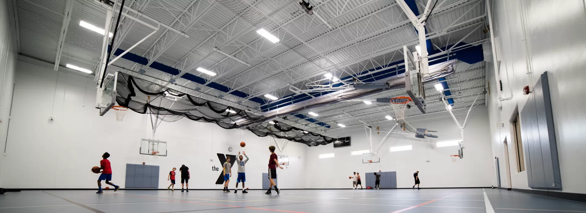 Large back gym with blue flooring and teenagers playing basketball
