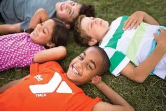 Kids in YMCA shirts laying in the grass