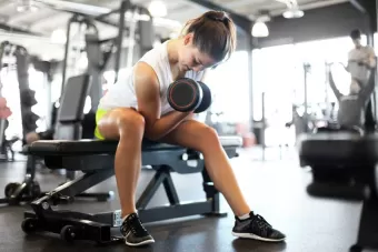 A women lifting weights while she sits on a bench in the gym.