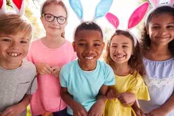 A group of kids with easter bunny ears on, smiling.